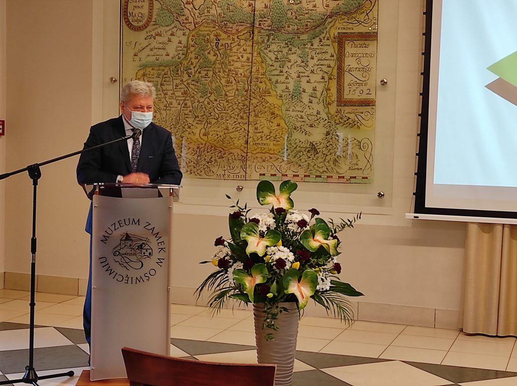 Przy mównicy stoi burmistrz Chełmka. W tle historyczna mapa , obok kwiatowa kompozycja w wazonie