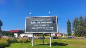 Billboard na czarnym tle biały napis: Tworząc wadliwe prawo rząd PiS pozbawił miasto Oświęcim 11 mln złotych znajduje się przy jednej z dróg wlotowych do miasta