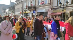 Oświęcimianie maszerują ulicą miasta z biało czerwoną biało-czerwoną flagą