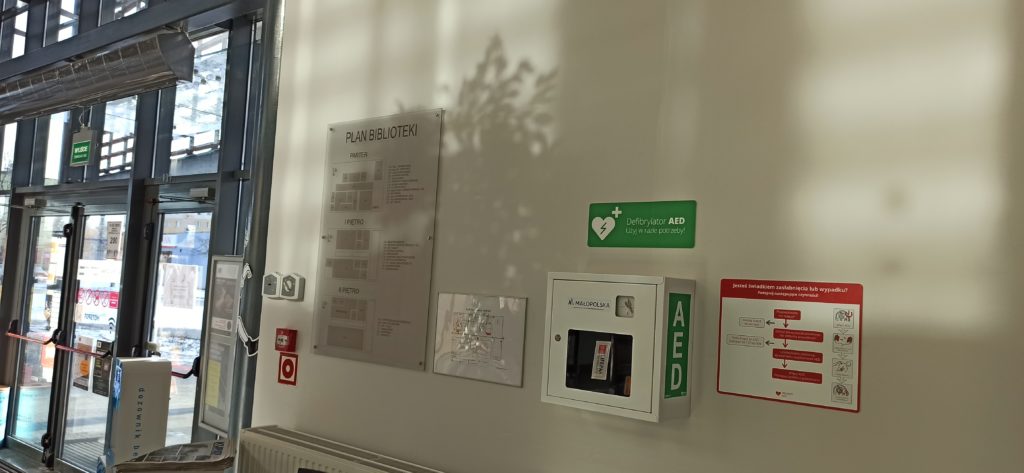 Defibrylator umieszczony w specjalnej  obudowie wisi na jednej ze ścian biblioteki