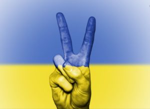 Dłoń z palcami w geście solidarności na tle niebiesko-żółtej flagi Ukrainy