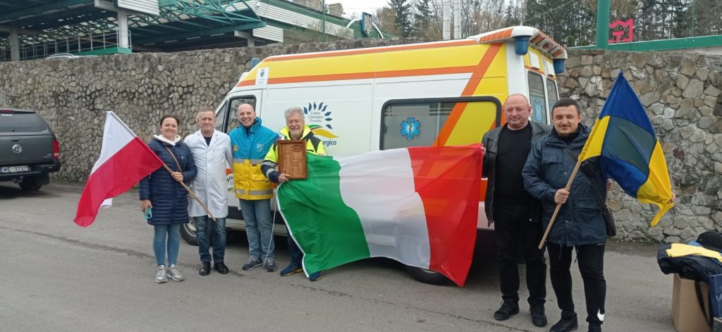 Na tle karetki stoją przedstawiciele Arezzo i Oświęcimia z flagą włoską, ukraińską i polską