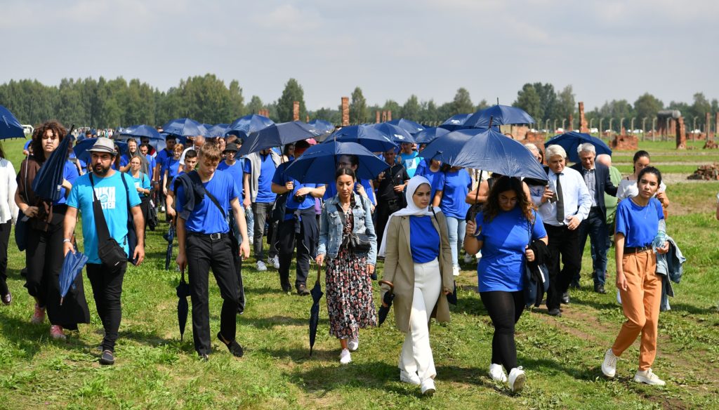 Grupa Sinti i Romów na terenie Muzeum Birkenau w drodze do miejsca, w którym upamiętniono ofiary narodowości romskiej