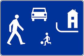 Znak drogowy informujący kierowcę, że znajduje się w strefie zamieszkania. Na niebieskim tle jest postać dziecka, dorosłego, samochód i dom