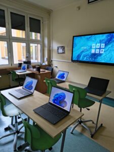 Pracownia sztucznej inteligencji - biurka na których znajdują się laptopy, na ścianie znajduje się monitor interaktywny